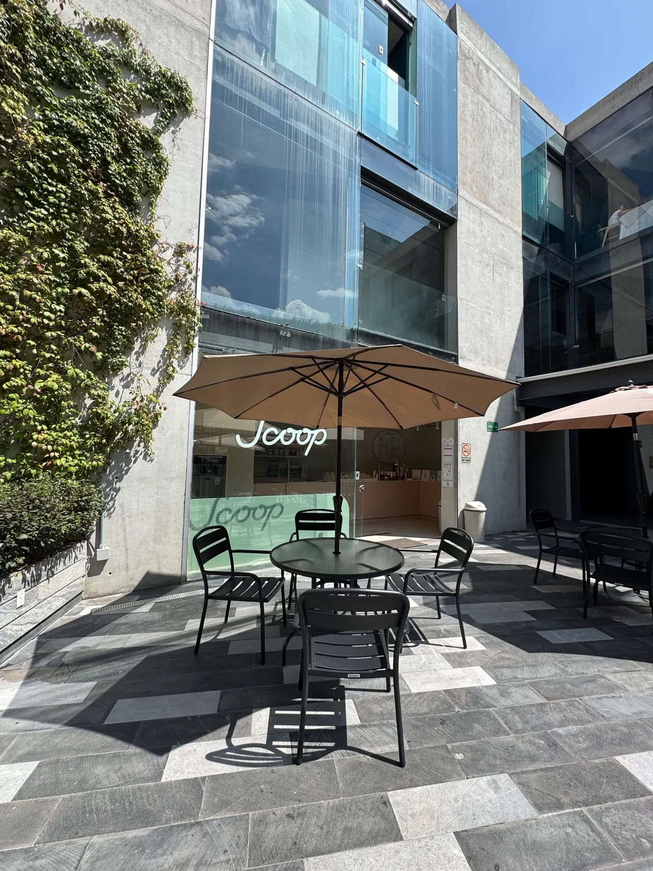Fachada de Scoop con una mesa y sombrilla en la terraza, bajo la fachada de cristal